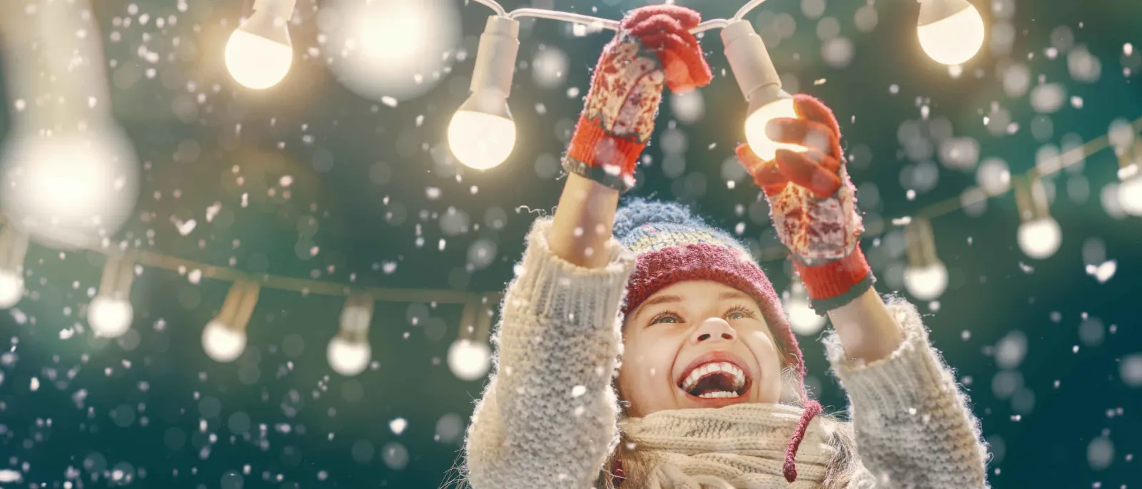 Ein Mädchen mit einer Lichterkette im Schnee.