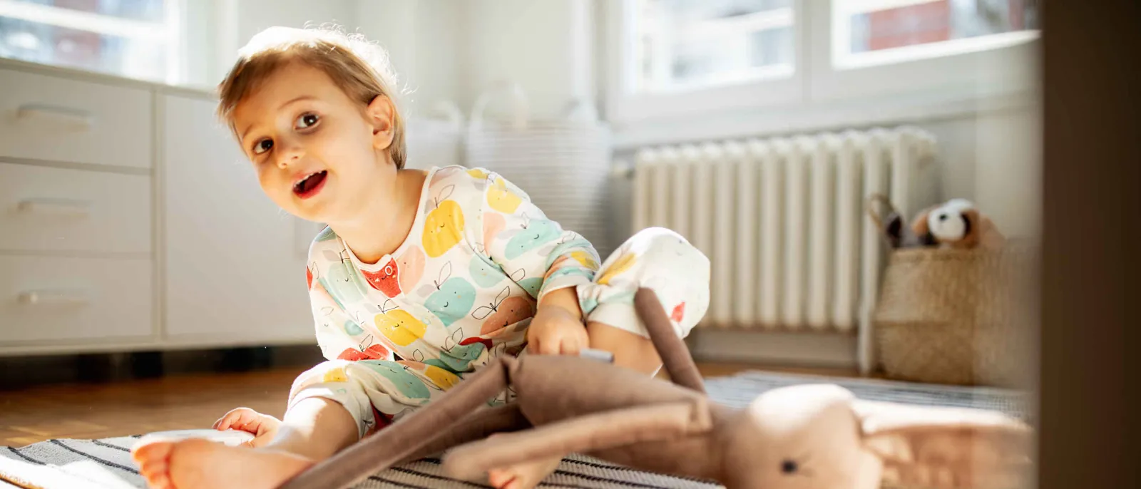 Ein Kleinkind sitzt mit nackten Füßen auf dem Fußboden.