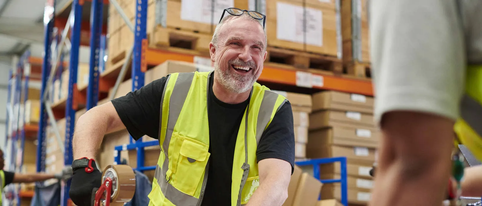 Ein Mitarbeiter im Lager trägt eine gelbe Weste und lacht.