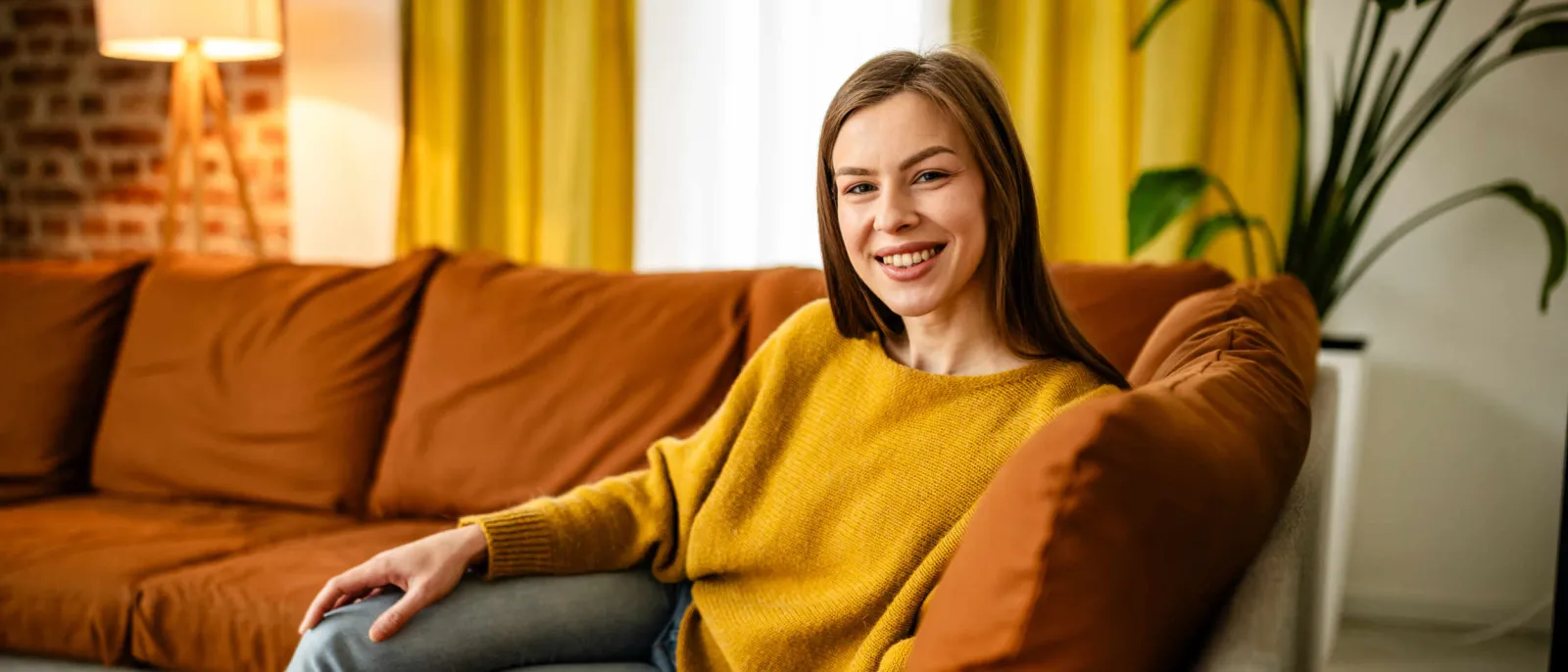 Eine Frau sitzt gemütlich auf dem Sofa und lächelt.