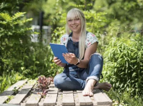 Eine Frau sitzt mit einem Tablet im Garten.