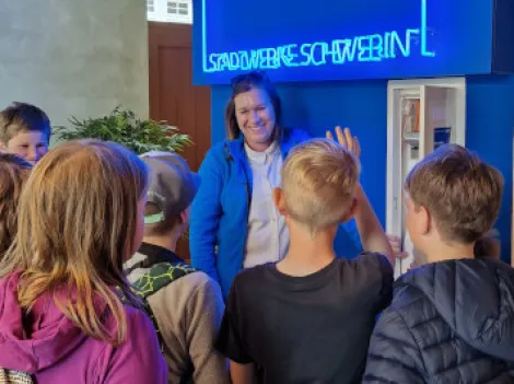 Eine Gruppe Schüler mit einer Stadtwerkemitarbeiterin am Medienschrank.