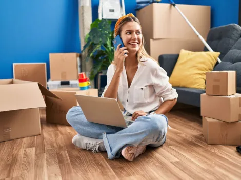 Eine junge Frau mit Laptop und Handy zwischen Umzugskartons.