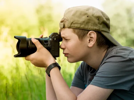 Ein Junge fotografiert draußen etwas mit einer Kamera.
