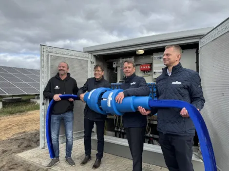 Vier Männer stehen vor einem Trafoschrank und halten einen großen Stromstecker 