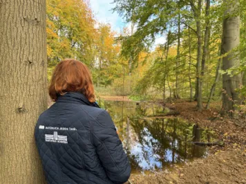 Eine Stadtwerkemitarbeiterin lehnt sich an einen Baum.