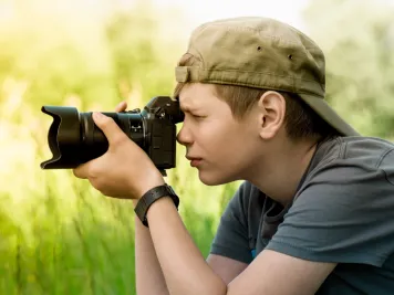 Ein Junge fotografiert draußen etwas mit einer Kamera.