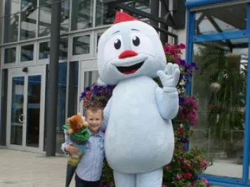 Junge mit Schultüte steht neben blauem Maskottchen