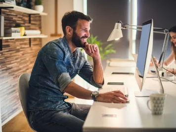 Ein Mann sitzt lächelnd vor einem PC.