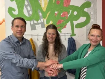 Zwei Frauen und ein Mann legen symbolisch die Hände aufeinander