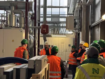 Ein Stadtwerkemitarbeiter mit typischer Arbeitsbekleidung steht im Heizkraftwerk und gibt Auskunft bei einer Führung.