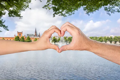 Eine Männerhand und eine Frauenhand formen ein Herz vor dem Hintergrund des Pfaffenteiches in Schwerin.