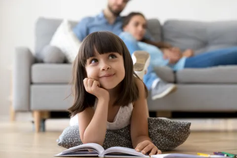 Ein kleines Mädchen liegt mit einem Buch auf dem Fußboden und schaut verträumt.