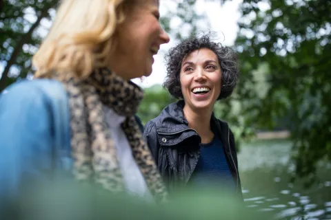 Zwei Freundinnen gehen im Wald spazieren und lächeln sich an.