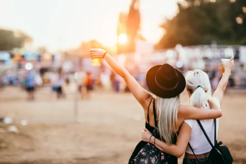 Zwei Frauen feiern am Strand. Beide halten ein Getränk in der Hand.