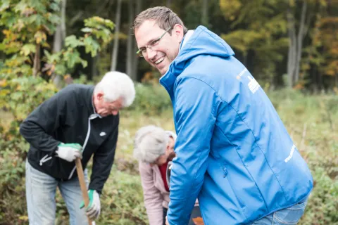 Ein Stadtwerke-Mitarbeiter und zwei weitere Personen pflanzen im Wald Baumsetzlinge ein.