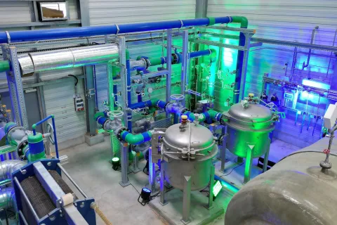 Innenaufnahme des SWS Geothermie-Heizwerks in Schwerin. Zu sehen sind mehrere Kessel, Rohre und Pumpen in beleuchteter Umgebung.
