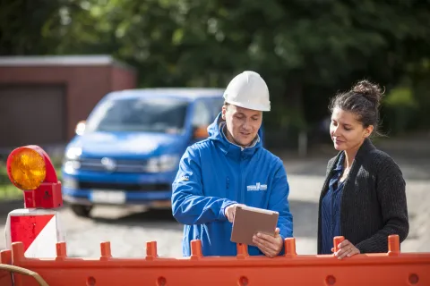 Ein SWS-Mitarbeiter zeigt einer Frau Informationen auf einem Tablet-PC. Sie stehen an einer Baustelle.