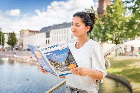 Eine junge Frau liest ein Stadtwerke-Magazin am Schweriner Pfaffenteich.