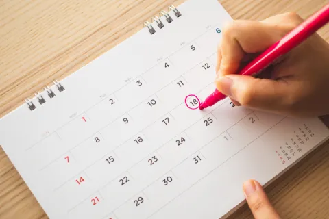 Eine Hand markiert einen Termin im Kalender.