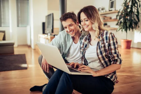 Ein Mann und eine Frau sitzen mit einem Laptop auf dem Sofa.