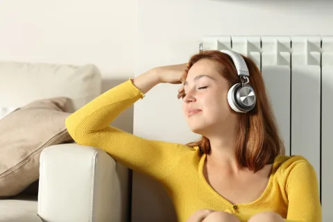 Eine Frau lehnt entspannt an der Heizung und hört Musik.