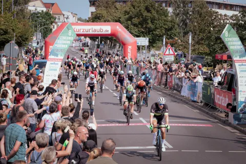 Eine große Gruppe von Sportfahrradfahrern auf der Rennstrecke gesäumt mit Zuschauern.
