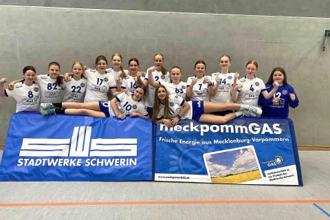Mannschaftsfoto von Frauen in Meckpommgas-Trikots, im Vordergrund Banden mit Logo Stadtwerke Schwerin und MeckpommGas.