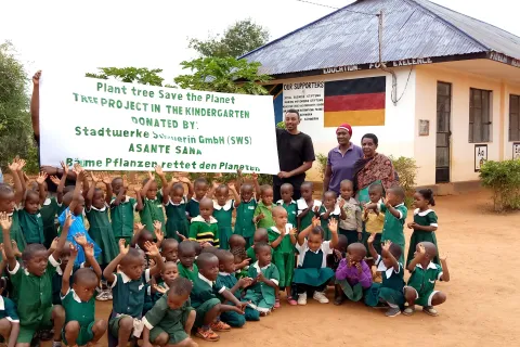 Eine Gruppe von afrikanischen Kindern in Schuluniform sitzt vor einem Banner mit Dankesgruß an die Stadtwerke Schwerin.