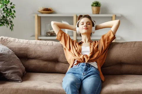 Eine junge Frau sitzt entspannt mit Kopfhörern auf dem Sofa.