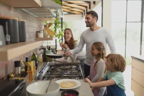 Familie steht am Gasherd und macht Pfannkuchen