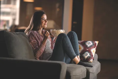 Eine Frau sitzt auf dem Sofa mit Popcorn in der Hand und schaut einen Film in der Nacht.