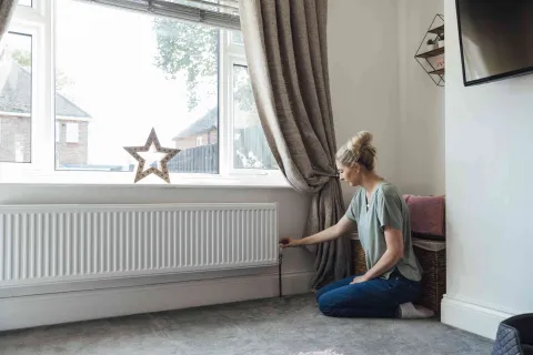 Frau dreht am Heizungsthermostat, um Energie zu sparen.