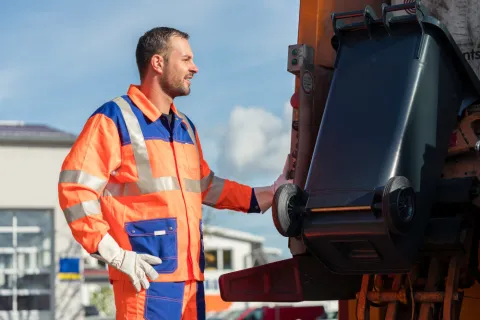Ein Mann leert Abfalltonne im LKW.