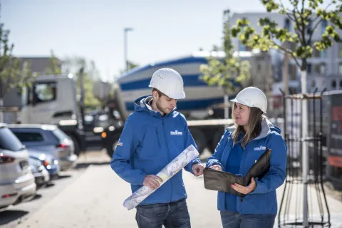 Zwei Stadtwerke-Mitarbeiter beraten sich auf einer Baustelle.