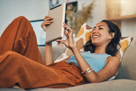 Eine Frau surft mit ihrem Tablet auf ihrem Sofa.