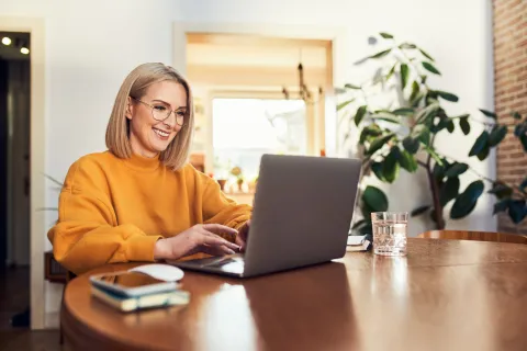 Frau sitzt zuhause am Tisch mit Laptop