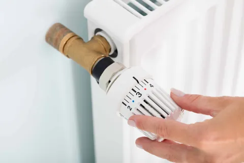 Frau dreht am Heizungsthermostat