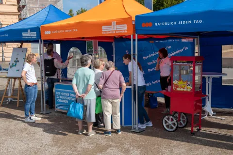 Stadtwerke-Pavillons mit Stehtischen, Aktionen und Mitarbeitenden. Davor steht eine Gruppe interessierter Passanten.