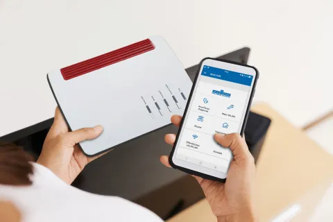 Eine Person hält einen Router und ein Smartphone in der Hand.