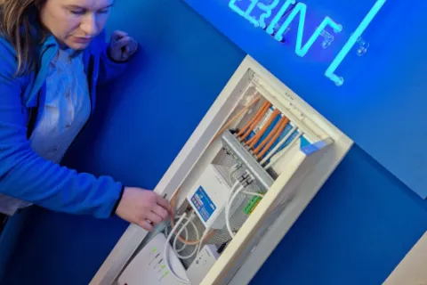 Eine Stadtwerke-Mitarbeiterin erklärt die Technik eines Medienschranks für das Glasfaser-Internet.