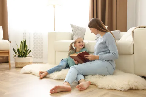Eine Frau sitzt mit ihrer Tochter auf dem Boden und liest ihr vor.