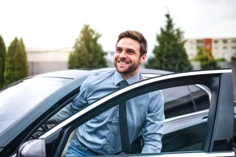Ein junger Mann mit blauem Hemd, der in der Stadt aus dem Auto steigt.