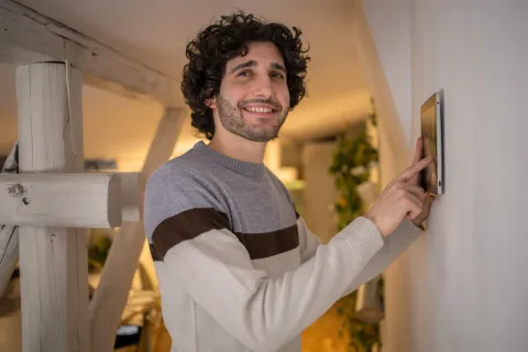 Ein junger Mann stellt die Temperatur zu Hause mit einem Gerät an der Wand ein.