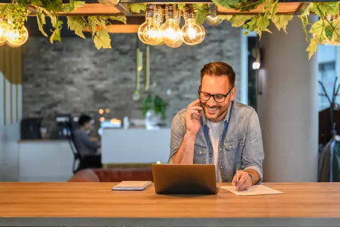 Ein Mann sitzt im Büro vor einem Laptop und telefoniert.