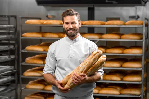 Bäcker steht vor seinen gebackenen Broten, die im mit Gas betriebenen Ofen gebacken wurden.