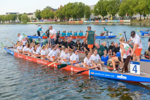 Drei Drachenboote legen ab, alle Teams haben einheitliche Shirts. 