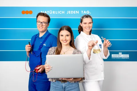 Drei Azubis der Stadtwerke Schwerin stehen vor einer blau gestreiften Wand.