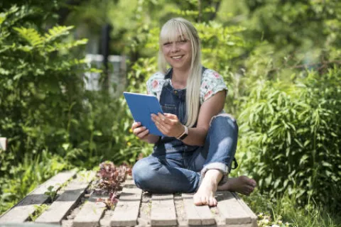 Eine Frau sitzt mit einem Tablet im Garten.