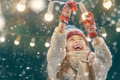 Ein Mädchen mit einer Lichterkette im Schnee.